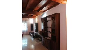 Amplia sala de estar con techo de madera, estantería empotrada y zona de comedor con mesa y sillas.