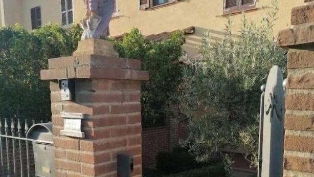 Puerta de ladrillo con una verja metálica, un buzón y una pequeña estatua en la parte superior.