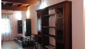 Amplia sala de estar con techo de madera, estantería empotrada y zona de comedor con mesa y sillas.