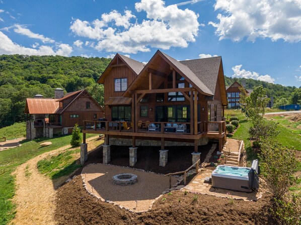 A large wooden cabin with multiple decks and a hot tub in the yard.