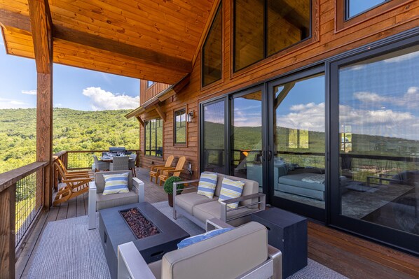 A wooden deck with outdoor furniture, large windows, and a scenic view of green hills.