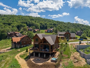 A cluster of wooden cabins with a hot tub and a deck, surrounded by lush greenery and hills.