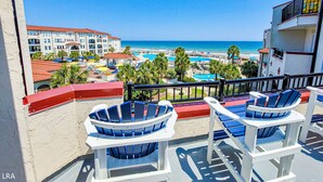 Un balcón con dos sillas Adirondack que da a una zona turística con varias piscinas, una playa y un edificio de hotel.