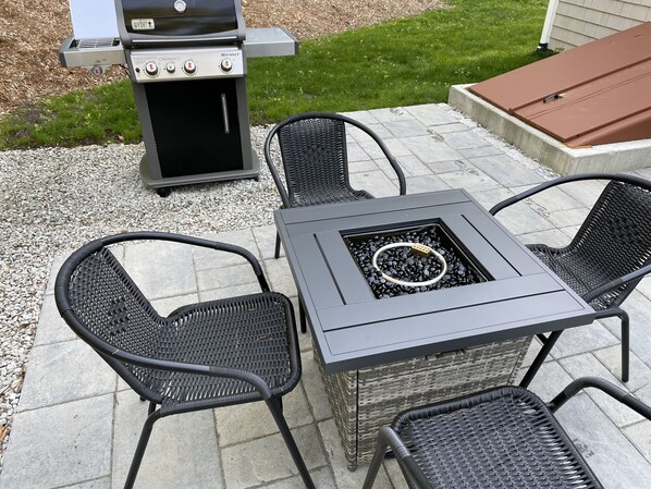 A patio with a grill, four wicker chairs, and a square table with a fire pit.