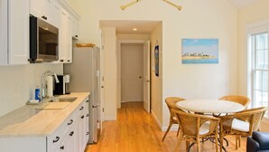 A kitchen with white cabinets, a microwave, and a coffee maker. There is a dining area with wicker chairs and a table. - New construction within 1 mile of bay beach and Nickerson Park (Brewster)