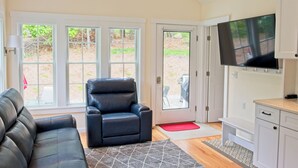 A living room with a black leather sofa, a black leather chair, a television, and a door leading outside. - New construction within 1 mile of bay beach and Nickerson Park (Brewster)