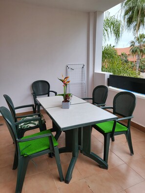 A balcony with a table and chairs, a potted plant, and a view of palm trees and buildings.
