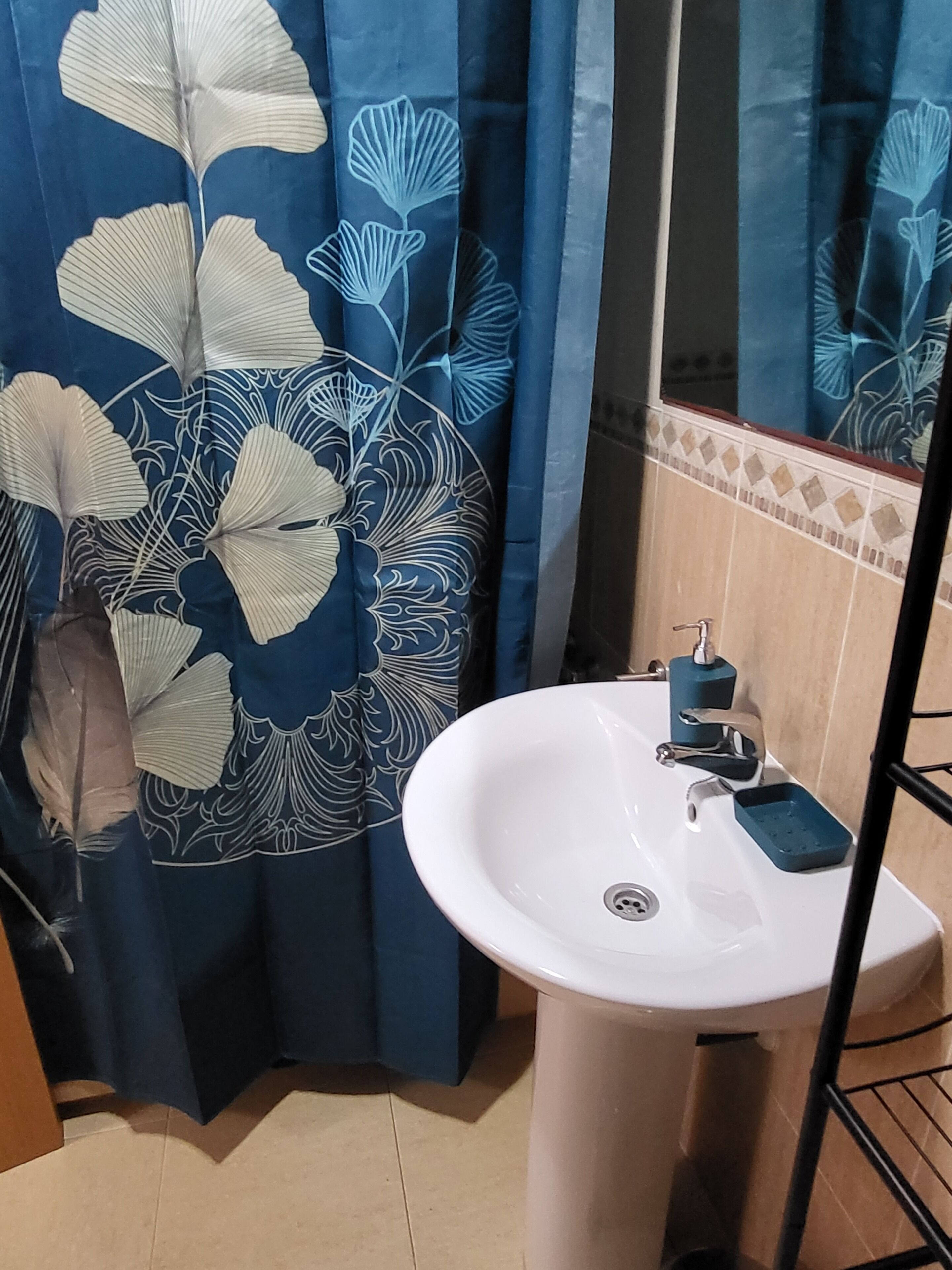 Ein Badezimmer mit einem weißen Waschbecken, einem blauen Duschvorhang mit Blumenmuster und einem gefliesten Boden.
