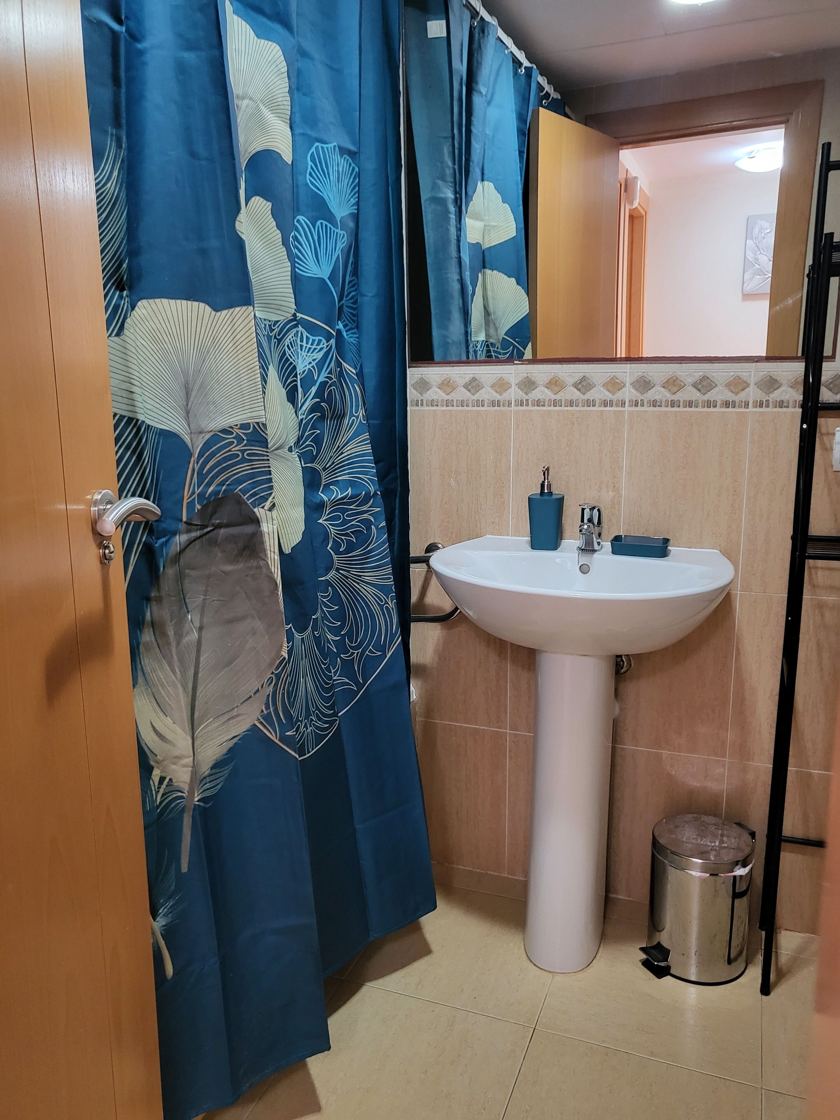 A bathroom with a white sink, a trash bin, and a shower curtain with a leaf pattern.