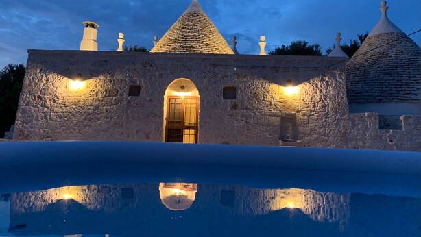 Un edificio de piedra con un arco central, varias chimeneas y una piscina que refleja la estructura.