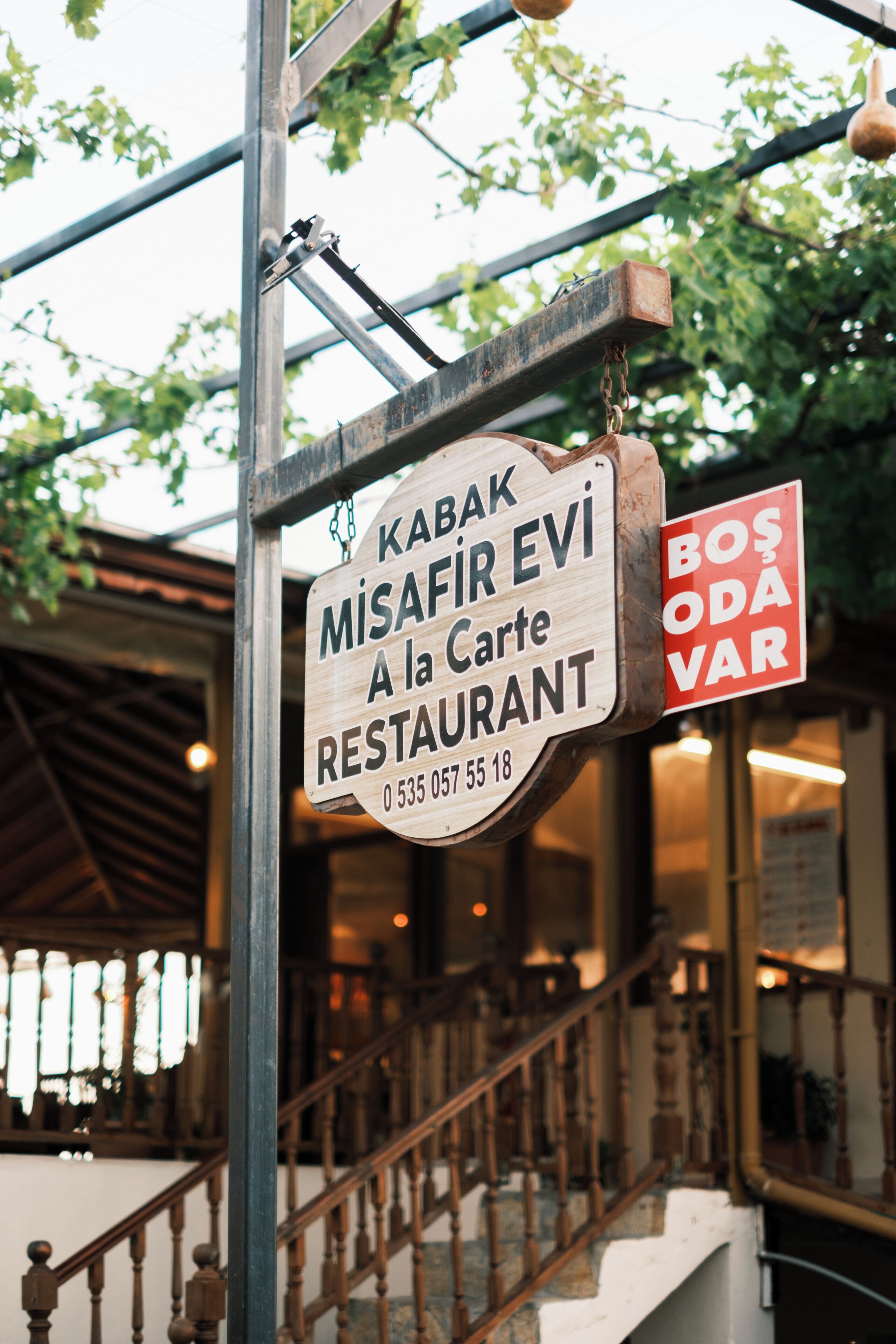 A wooden sign for a restaurant with a contact number.
