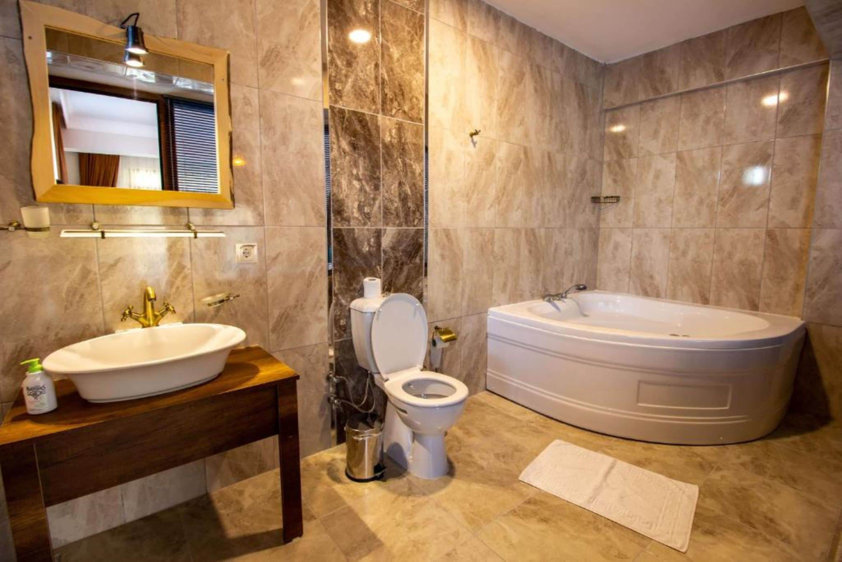 A modern bathroom with a marble wall, a freestanding bathtub, a sink with a mirror, and a toilet.