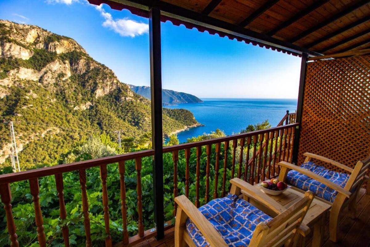 A balcony with a wooden railing, blue patterned cushions, and a table with fruit.