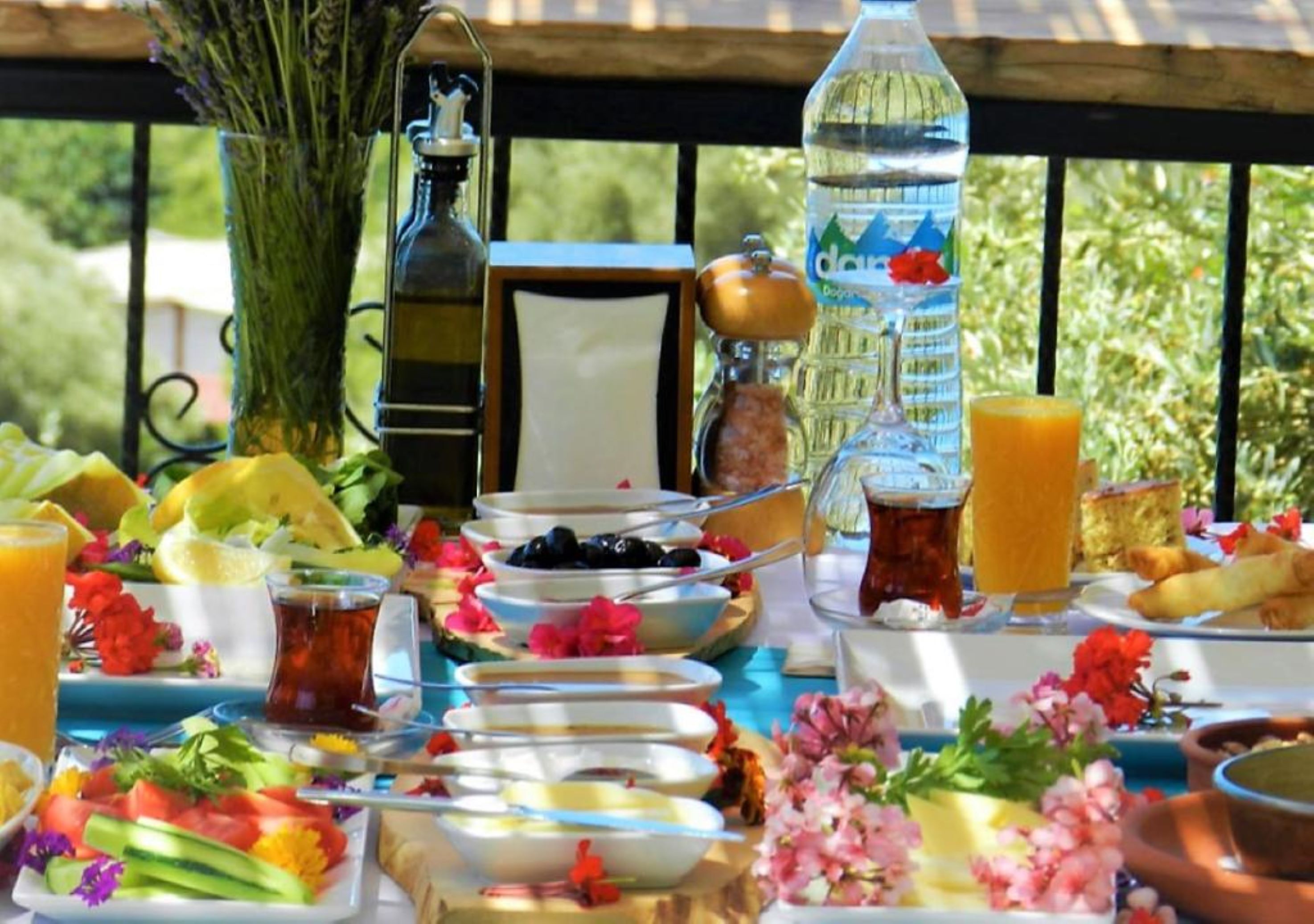 A table set with various dishes, a bottle of water, and a glass of juice, likely in an outdoor dining area.