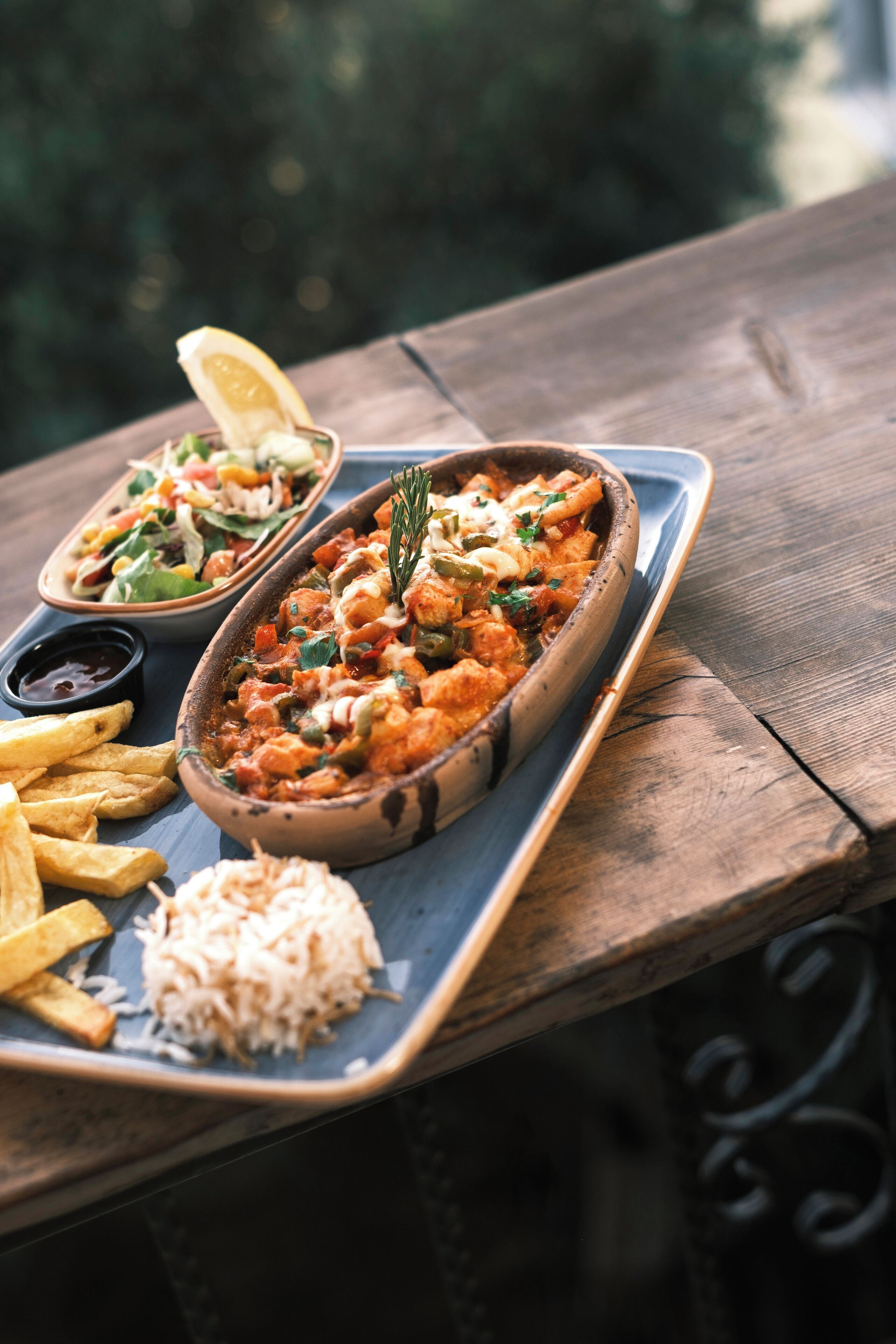 A wooden table with a dish of food, a bowl of rice, and a small bowl of sauce.