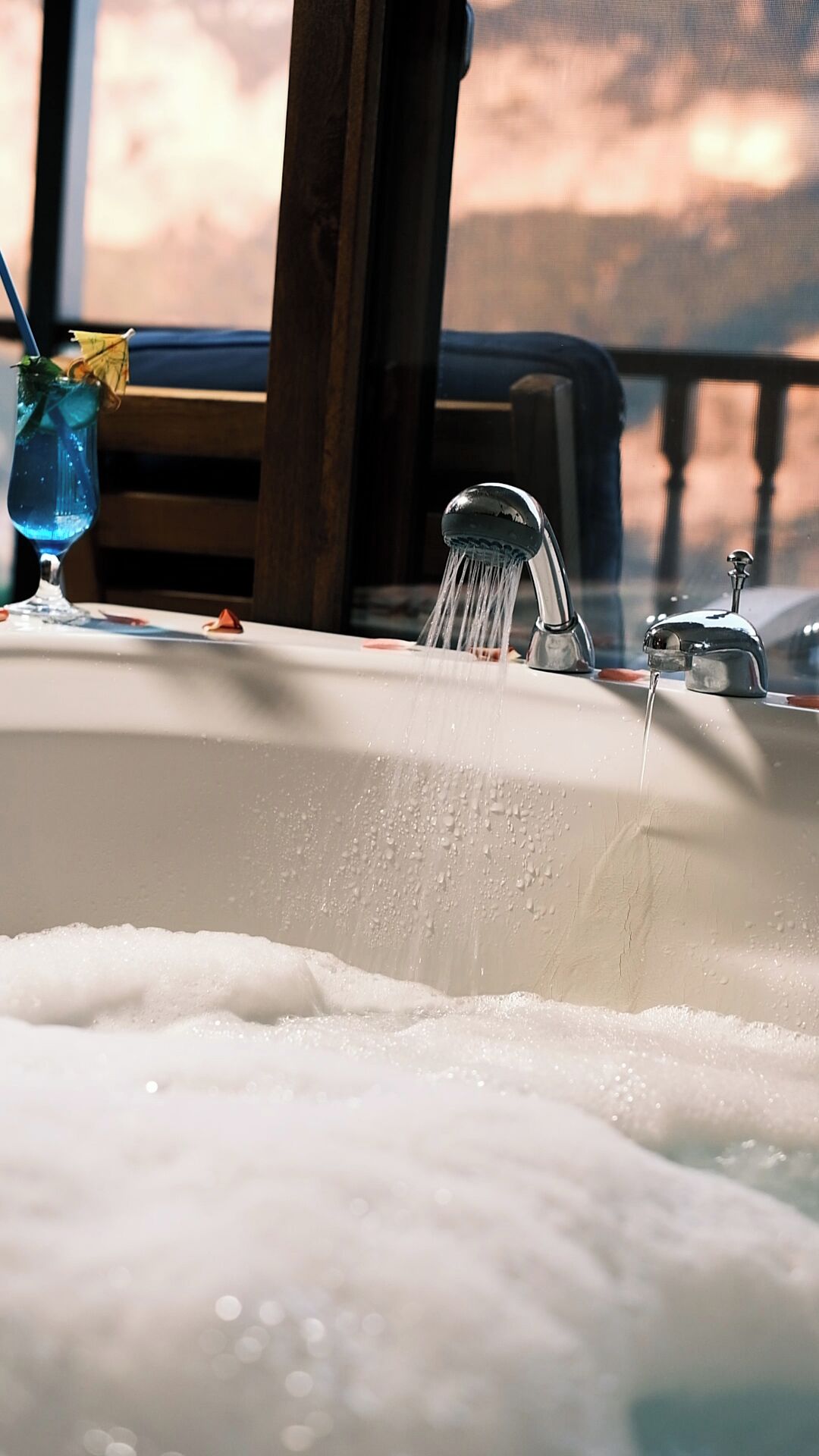 A bathroom sink with running water, a glass of water, and a window in the background.