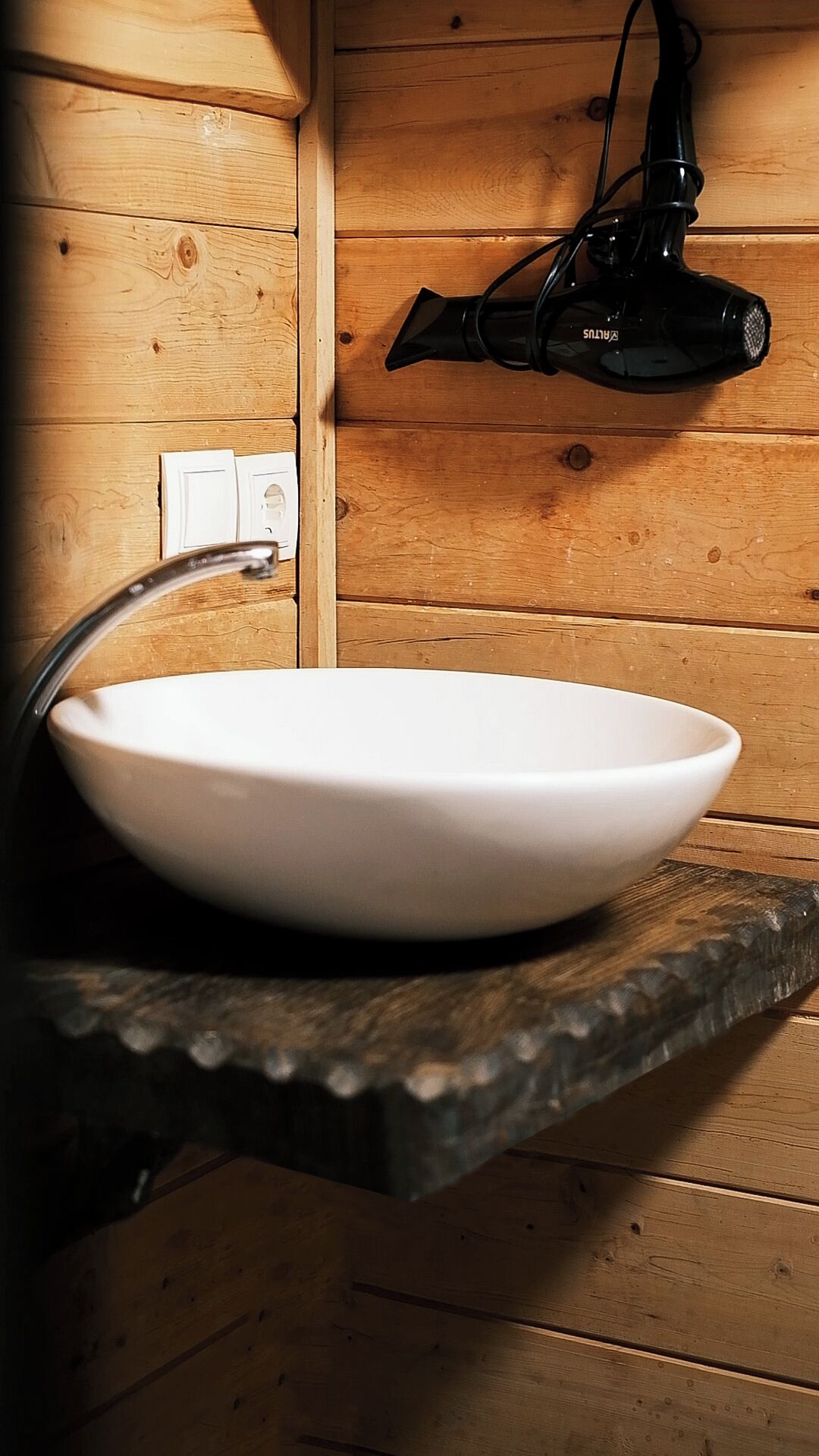 Un évier en céramique blanche, doté d’un robinet moderne, dans une salle de bain aménagée dans le style d’un chalet en bois.