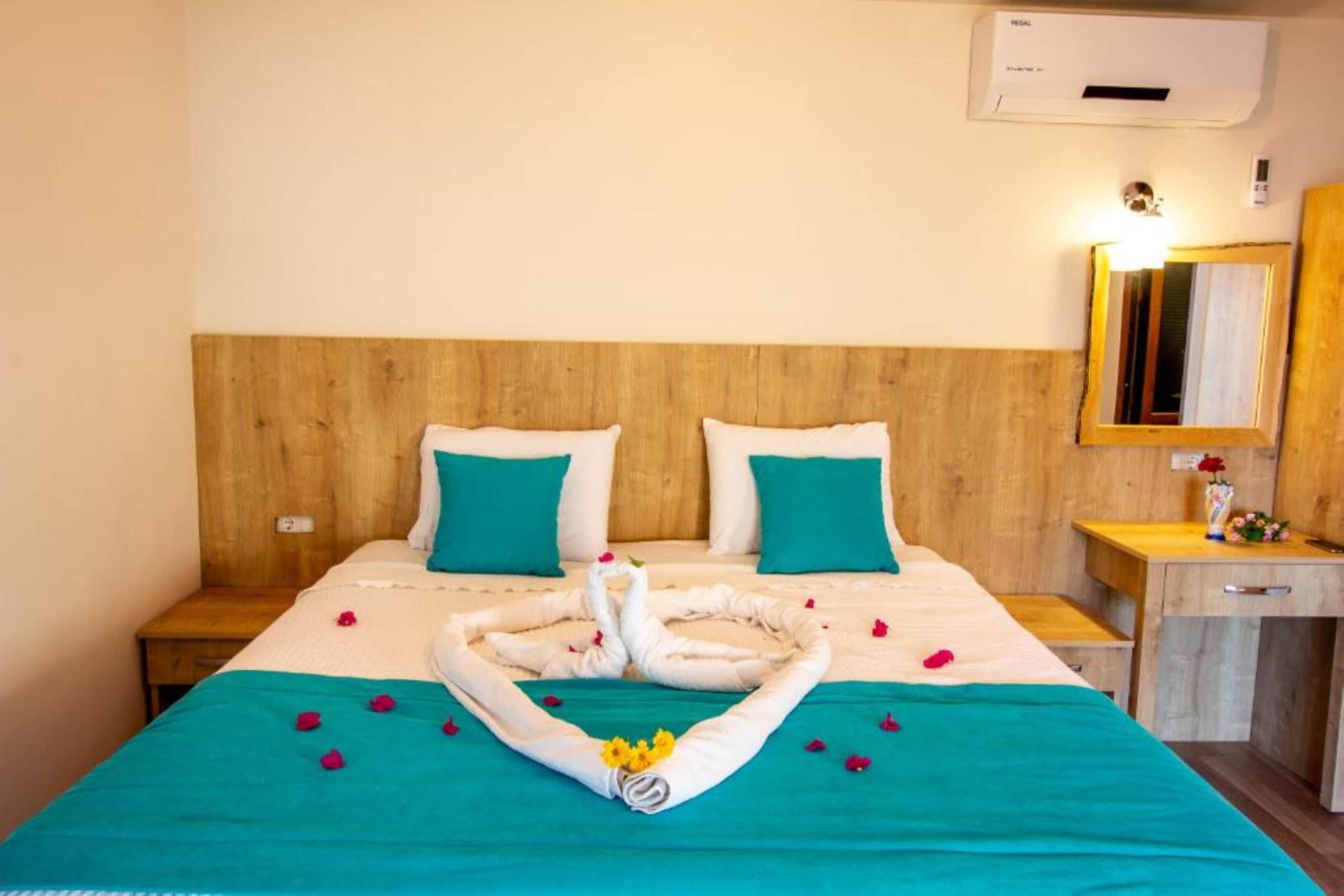A hotel room with a wooden headboard, teal bedding, and a swan towel arrangement on the bed.