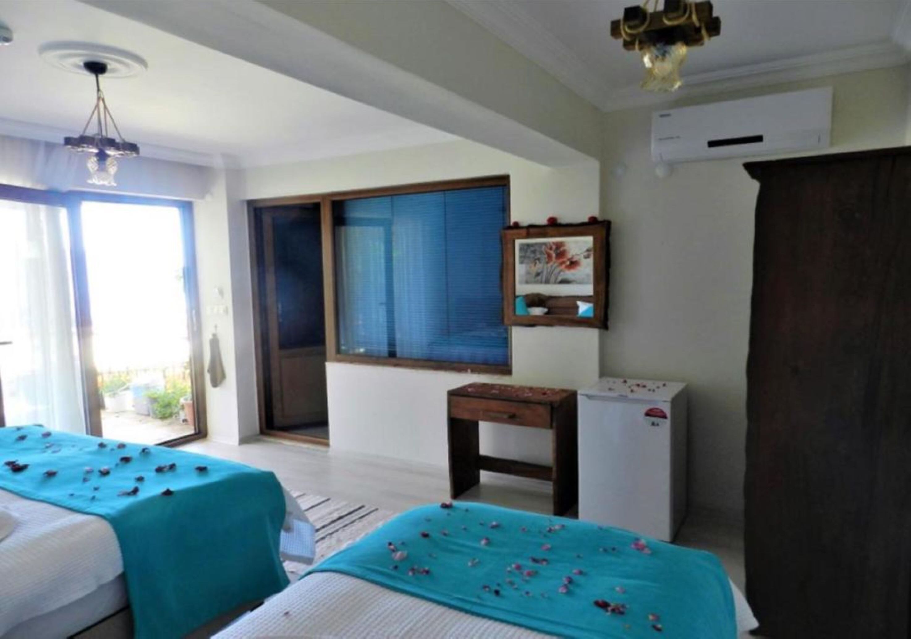 A hotel room with two beds, a small table, a window with blinds, and an air conditioning unit.