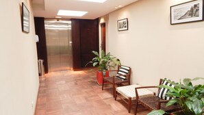 Un pasillo con suelo de madera, dos sillones con cojines y plantas en macetas.