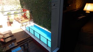 Zona de piscina exterior con terraza de madera, sillas de descanso y vistas a un edificio con pared verde.