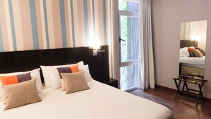 Una habitación de hotel con una cama grande, pared a rayas y una ventana con cortinas.