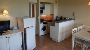 A compact kitchen with a washing machine, microwave, and a small dining area with chairs. - Residence LE HAMEAU DES ISSAMBRES (Les Issambres)