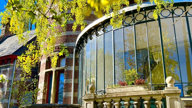 Un edificio histórico con fachada de cristal curvo, paredes de ladrillo y un balcón con barandilla.