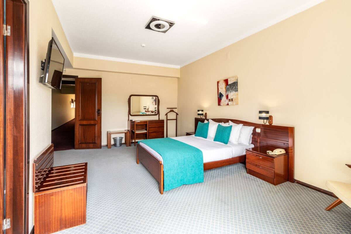 A hotel room with a bed, bedside table, nightstand, and a mirror.