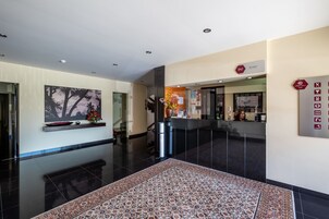 Un moderno vestíbulo de hotel con una mesa de recepción, un cuadro abstracto de gran tamaño, un letrero de recepción y una alfombra estampada.