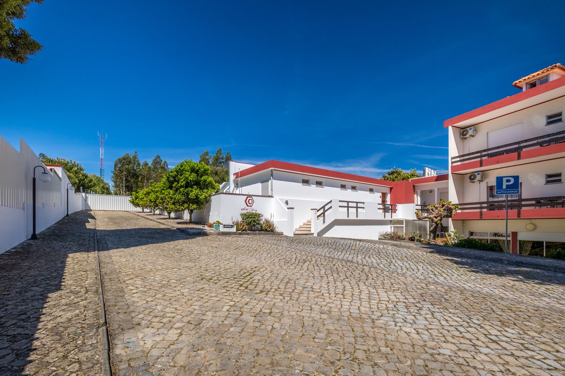 Une rue pavée menant à un bâtiment avec un toit rouge et des murs blancs, un panneau indiquant un parking et un ciel bleu dégagé.