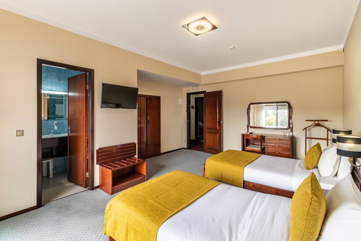 A hotel room with two beds, a desk, a mirror, and a bathroom visible through an open door.