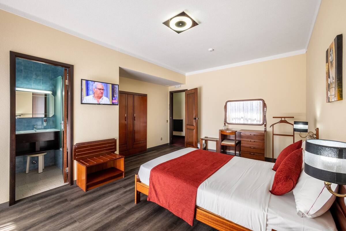 A hotel room with a bed, a desk, a chair, a wardrobe, a mirror, and a television.