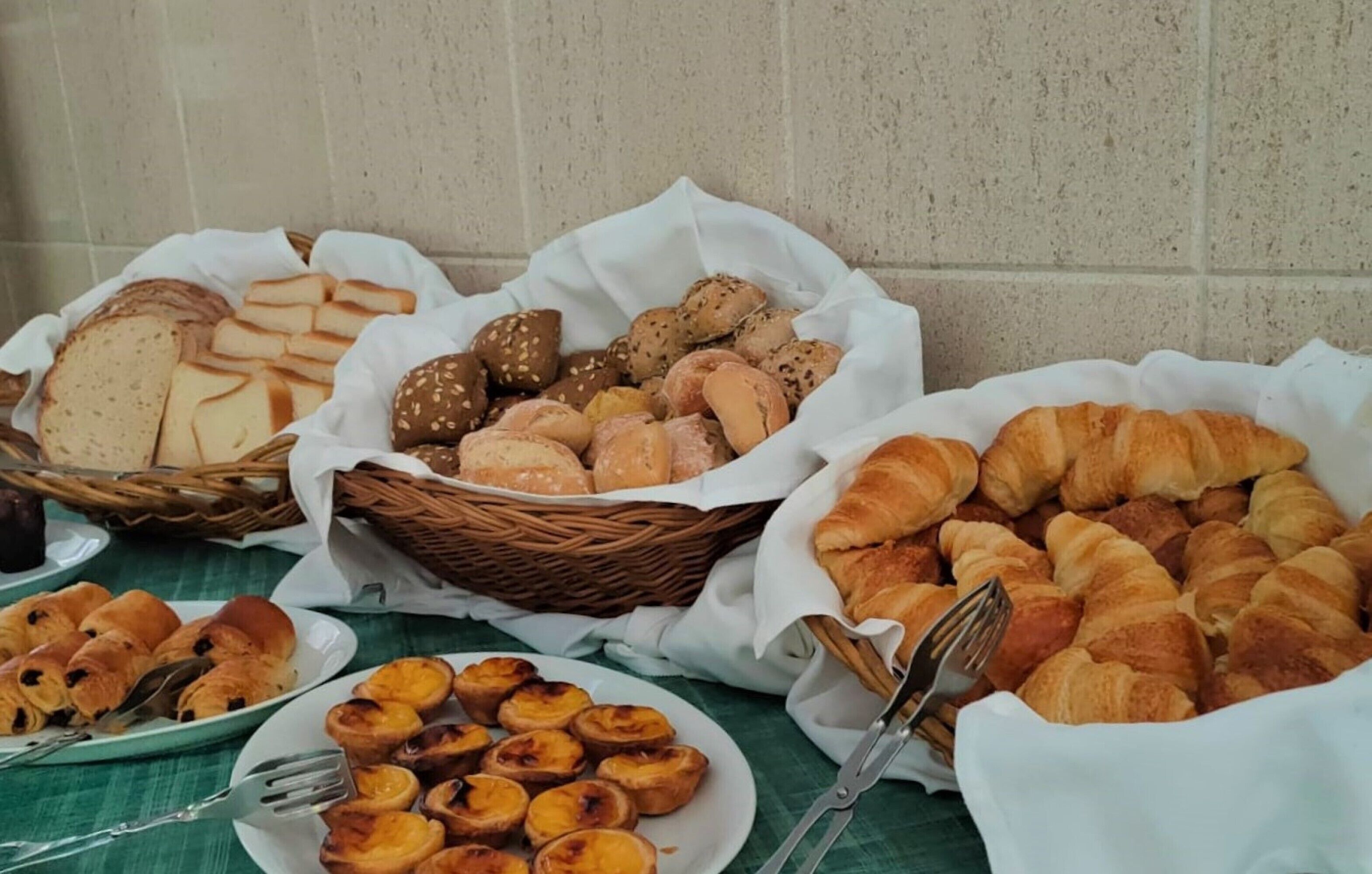 A variety of baked goods including bread, croissants, and pastries arranged on a table with a green tablecloth.