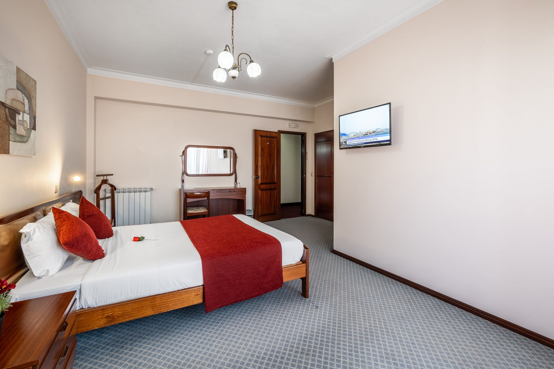 Habitació d'hotel amb un llit, una petita arca de fusta, un mirall, un televisor i un radiador.