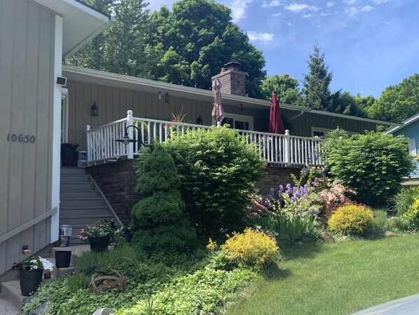 A house with a covered porch, a brick chimney, and a garden with various plants and flowers. - Perfect Getaway - 5 min walk to beach, Tart trail, boat/kayak launch (Traverse City)