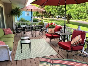 Eine überdachte Terrasse im Freien mit einem grünen Sofa, roten Stühlen, einem Tisch und einem gemusterten Teppich.