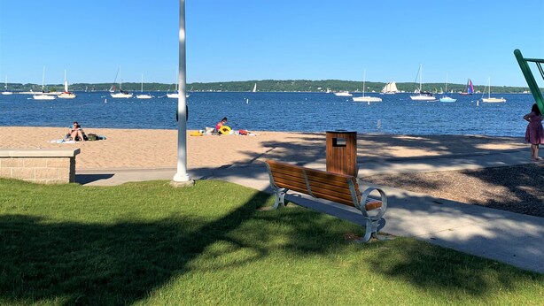 Un parque con un banco, un farol y vistas al agua con barcos.