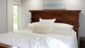 Una cama bien hecha con cabecera de madera, ropa de cama blanca y un cuadro en la pared.