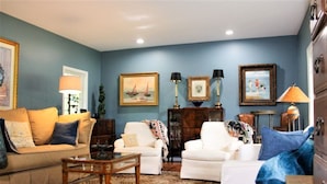 Una sala de estar con una pared azul, un sofá color beige, un sillón blanco, una mesa de centro y un tapete estampado.
