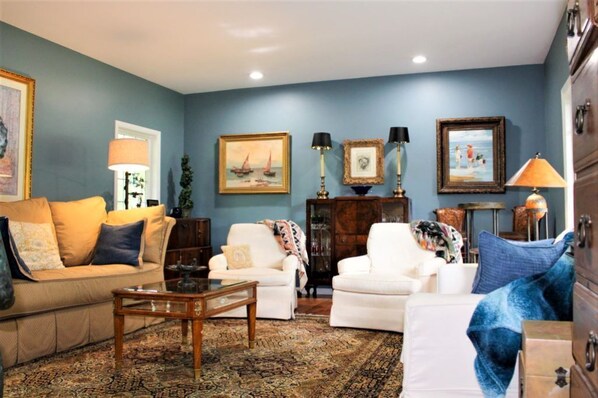 Ein Wohnzimmer mit blauer Wand, einem beigen Sofa, einem weißen Sessel, einem Couchtisch und einem gemusterten Teppich.