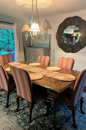 Ein Esszimmer mit Holztisch, karierten Stühlen, gewebten Platzsets und einem Kronleuchter.