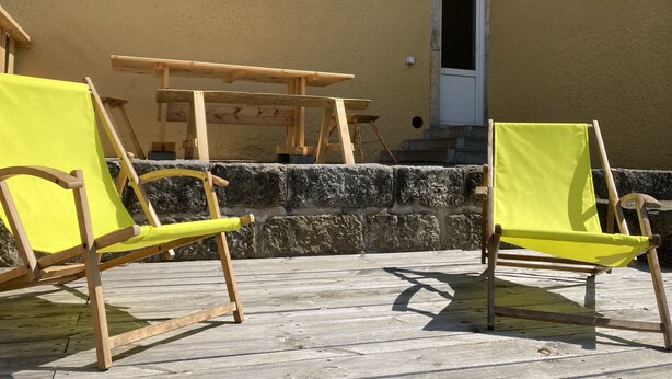 Une terrasse en bois avec deux chaises jaunes et une table en bois.
