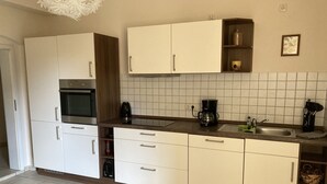Une cuisine moderne avec des meubles blancs, un four encastré, une machine à café et un évier.