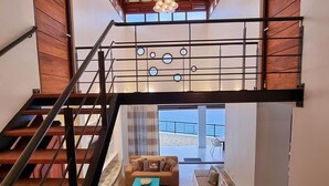 A spacious interior with a staircase leading to a balcony, a seating area with a sofa and coffee table, and a view of the outdoors. - Seafront Villa in Lagun Curaçao -pool-Wifi + With Private access to sea! (Lagun)