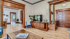 Ein geräumiges Wohnzimmer mit Holzböden, einem Fernseher und einem Essbereich mit Tisch und Stühlen.