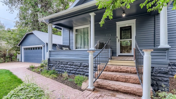 Ein zweigeschossiges Haus mit Natursteinfassade, einer Veranda mit Treppe und einer Garage.