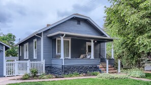 Ein zweistöckiges Haus mit Veranda, weißem Zaun und Steinunterbau.