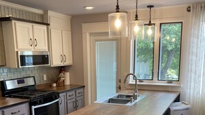 A modern kitchen with a central island, stainless steel appliances, and a window with a view of greenery. - Downtown Boyne City. Great Backyard  (Boyne City)