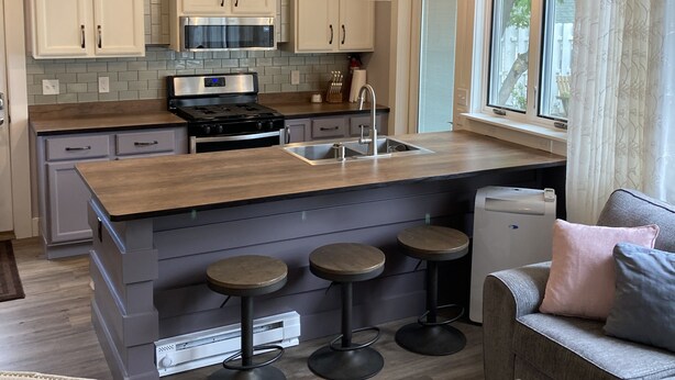 A modern kitchen with white cabinets, a central island with stools, a built-in oven, and a ceiling fan. - Downtown Boyne City. Great Backyard  (Boyne City)